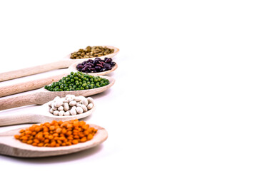 Row of wooden spoons filled with colorful legumes on white background. Variety of beans, lentils and peas arranged diagonally. Healthy vegetarian food, plant protein concept.