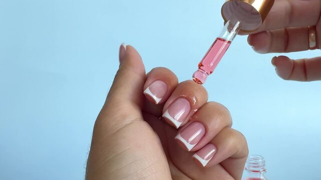 Moisturizing pink oil for cuticles. The woman cares for hands and nails, close up. Woman applying oil from pipette to cuticle on light background, macro. Healthy nails concept.