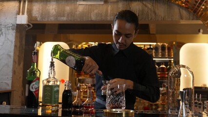 Portrait good looking Asian bartender using jigger measure liquor syrup into mixing glass preparation at luxurious beverage counter bar, neat professional barman costume at nightclub luxury. Vinosity.