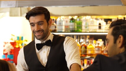Good looking bartender warm smiling friendly conversation with couple customer at beverage bar counter while serving welcome drink with charm professionalism recommending special menu list. Vinosity.