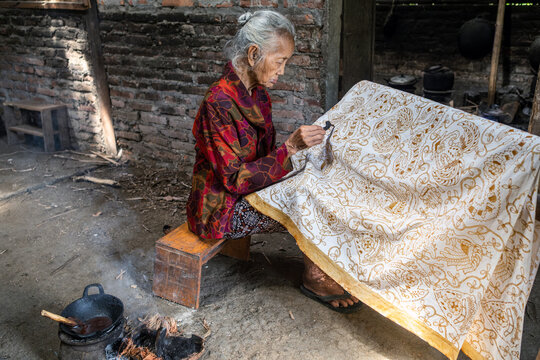 Indonesian woman making traditional batik fabric with canting tool