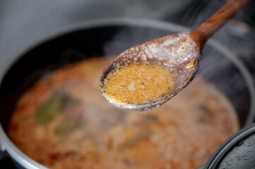 Top-down view of a pot filled with hearty soup, such as bograch or a creamy cheese-based soup. A wooden spoon rests over the pot, filled with steaming broth.