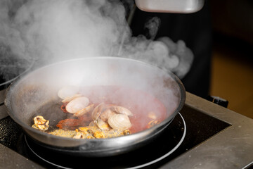 A close-up shot of a steaming pan with clams and mussels simmering in a rich tomato-based sauce. The image captures the freshness and vibrant colors of seafood cooking.
