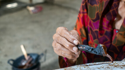 Indonesian artisan drawing batik traditional textile with canting tool