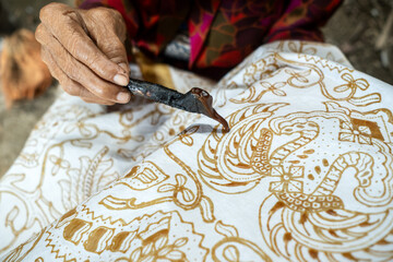 Artisan drawing traditional batik pattern on white cloth with canting tool