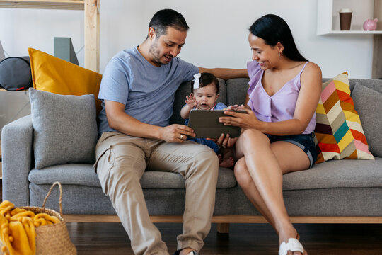 Hispanic family using tablet with baby daughter on sofa at home
