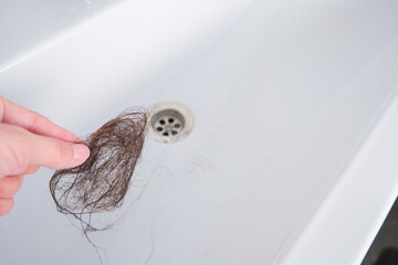A lot of loose female hair in the sink. A woman removes garbage from the sink