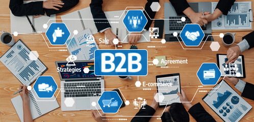 A dynamic business meeting focused on B2B strategies, featuring diverse professionals collaborating over laptops, charts, and innovative digital icons for modern commerce solutions. Amity