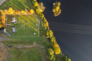 Small electrical substation near a river, surrounded by nature, with visible power lines and infrastructure