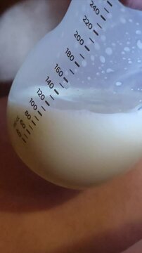 This close-up video shows a clear plastic bottle filled with pumped breast milk with measurement markings visible on the side. There are tiny bubbles in the creamy, clear liquid. 4k video