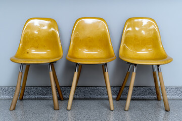 Three vintage yellow chairs with smooth, glossy surfaces and wooden legs are arranged in a straight line against a light gray wall, showcasing a minimalist design.