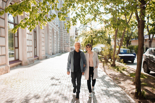 Senior happy couple of stylish man and woman 60-65 year old walking together on streets at city outdoors. Wellness lifestyle. Spring season.