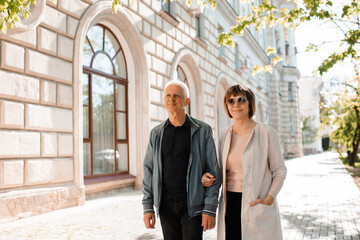 Senior happy couple of stylish man and woman 60-65 year old walking together on streets at city outdoors. Wellness lifestyle. Relationship.
