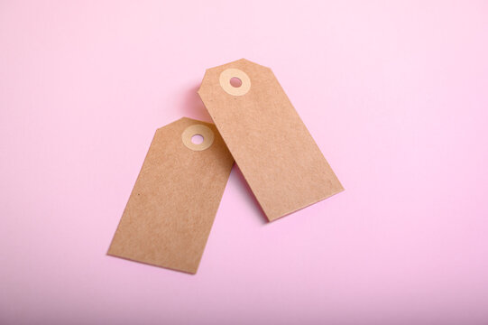 Two blank brown paper tags placed on a soft pink background ready for use in various crafts