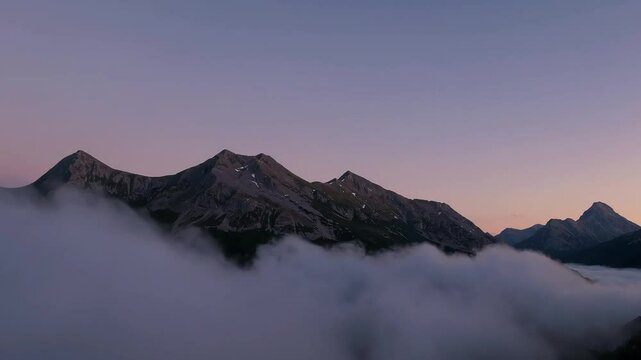 Mountain peaks rise above a soft blanket of clouds at dawn, evoking majesty and calm.