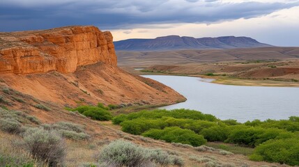 Obraz premium A scenic landscape featuring expansive red rock formations, a winding river, and lush green foliage under a dramatic sky, Perfect for travel, nature, or outdoor-themed projects,