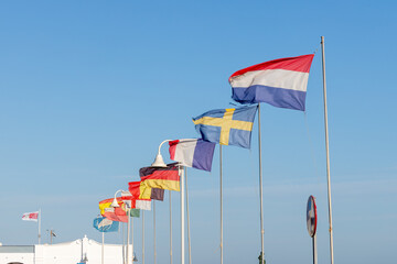 Colourful flags of different countries Denmark Germany Spain Belgium France flutter in the wind against a clear blue sky, symbolising international tourism and summer holidays.