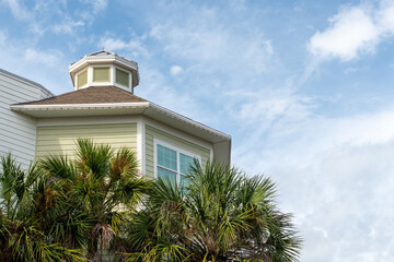 A small green and white cupola, a dome-like structure atop an octagon-shaped wooden building with pale green vinyl siding. There's a small glass pane window in the exterior wall with palm trees below.
