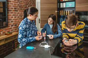 Smiling mother and daughter checking batteries to flashlight while son using portable radio...