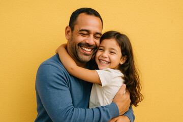 Father embraces daughter in front of yellow wall.