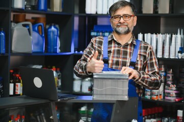 Salesman showing car battery and giving thumbs up in auto parts store