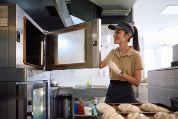 Happy female baker heating oven for baking pastry.