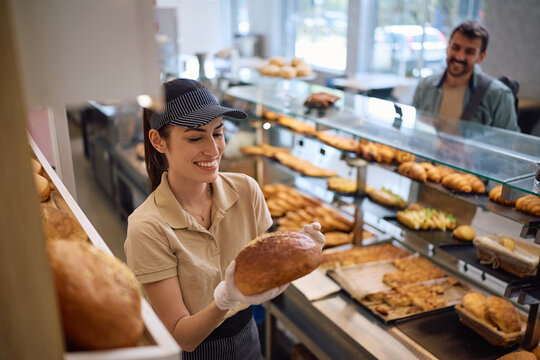 Happy female baker selling fresh bread to customer.