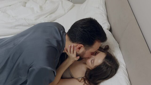 Romantic couple sharing intimate moments, kissing and embracing tenderly on comfortable bed, expressing love and affection in a cozy bedroom setting