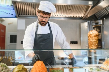 Chef arranging ingredients for shawarma or kebab in restaurant kitchen