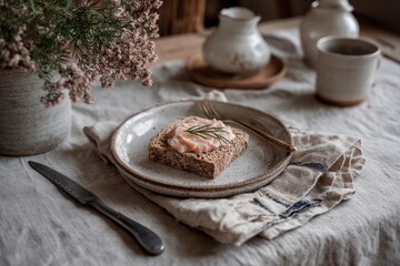 A rustic table is adorned with a slice of rye bread topped with salmon and a sprig of rosemary. Soft lighting highlights the calming ambiance of this inviting space