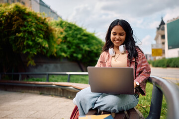 Happy Indian student e-learning over her laptop at campus.
