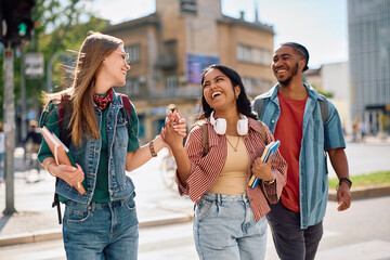 Multiracial group of cheerful college students communicating while walking down street. © Drazen