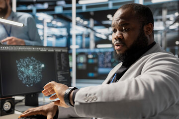 Admin in data center checking time during late shift while working on PC. Server room worker under deadline pressure inspecting settings and verifying final system configurations