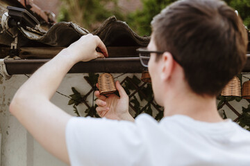 A young man hangs garland lights on a garden house.