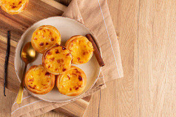 Pastel de Nata – Traditional Portuguese egg custard tarts arranged on the left side of a rustic wooden background. Plate composition leaves right space empty. Classic dessert from Portugal, top view