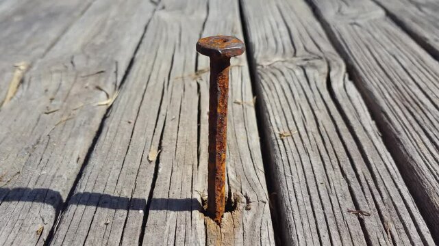 A nail sticking out of a wooden plank. The nail is rusty and has a shadow on the wood