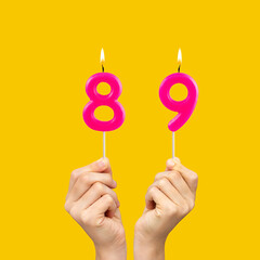 Hands holding birthday candles with number 89 - Yellow background