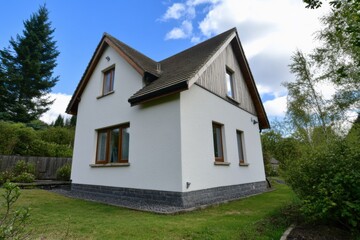 Modern white house surrounded by greenery, showcasing a well-maintained garden and a clear blue sky during a sunny day in the countryside