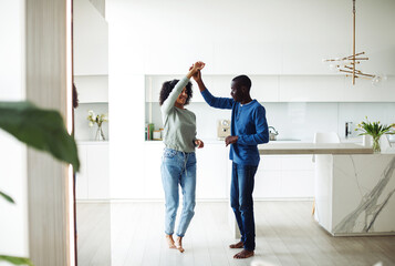 Cheerful black couple dancing to music in modern kitchen interior.