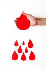 A female hand holding a big paper drop of blood and some smaller paper drops of blood on white...