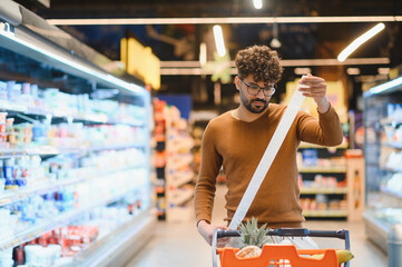 Shopper checking grocery receipt in supermarket: inflation and budgeting concept