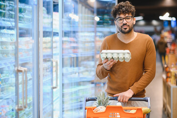 Arab man choosing eggs in supermarket refrigerator section