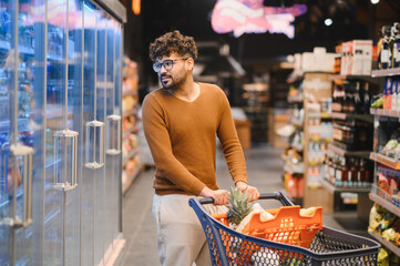 Arab man pushing shopping cart and choosing groceries in supermarket