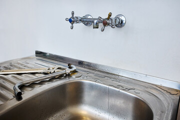 Stainless steel kitchen sink with detached faucet spout lying next to adjustable wrench and pipe...