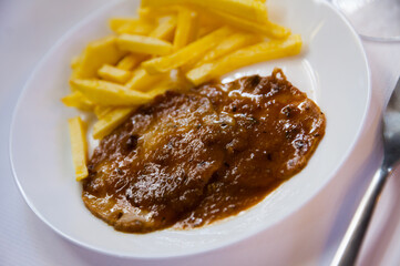 Slices of garlic crusted pork Carne Mechada with side dish of fried potato and sauce. Andalusian...