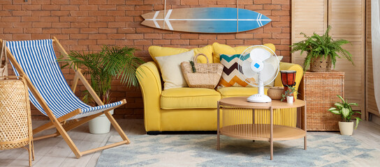 Interior of stylish living room with yellow sofa, surfing board and electric fan on coffee table