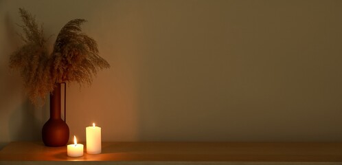 Burning candles and vase with grass on table in dark room. Banner for design