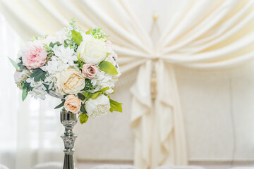 The central decoration of white and pink flowers stands on a silver stand on a decorated table and is part of a wedding or formal event, banquet hall