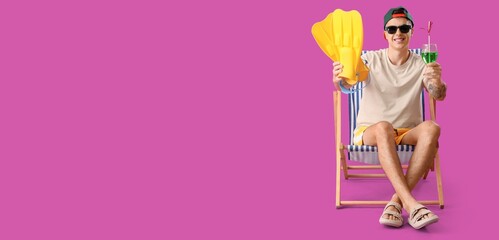 Young man with cocktail and flippers sitting on deck chair against purple background with space for text © Pixel-Shot