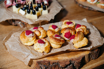 Mini Raspberry Cream Puffs on Rustic Tray. Close-up of mini cream puffs topped with raspberries, beautifully arranged on parchment and wood slices for a festive event.